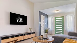 A modern living room with a flat-screen TV, a wooden console table, a round coffee table, and a sofa with a yellow throw blanket. - Your home away from home! (Round Rock)
