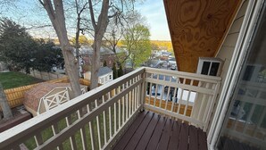 Eine Holzterrasse mit weißer Brüstung, die auf einen Garten mit Holzzaun und Bäumen blickt.