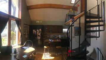 A kitchen with a bar area, wooden beams on the ceiling, and a staircase leading to an upper level.