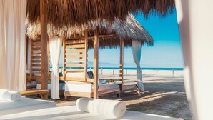 Eine Strandlounge mit Holzmöbeln, einem Reetdach und Blick auf das Meer.