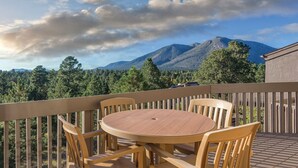 A wooden deck with a round table and chairs, overlooking a mountainous landscape with trees. - 2BD/Flagstaff - Full Kitchen, Living Room, W/D and Balcony! (Flagstaff)