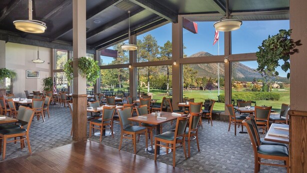 A spacious restaurant with wooden tables and chairs, large windows offering a view of a golf course and mountains. - 2BD/Flagstaff - Full Kitchen, Living Room, W/D and Balcony! (Flagstaff)