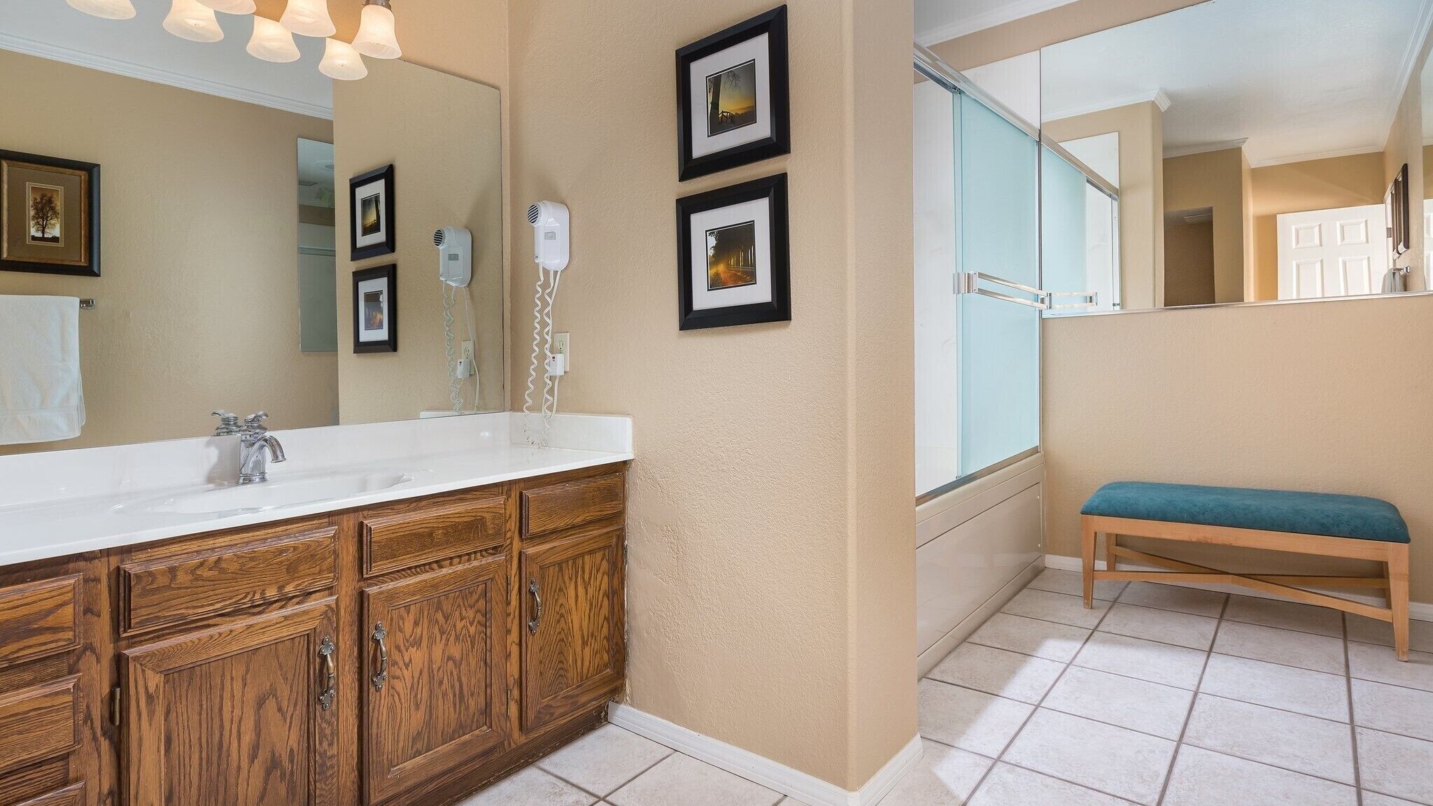 Une salle de bain avec un meuble-lavabo en bois, un grand miroir et des tableaux encadrés accrochés au mur.