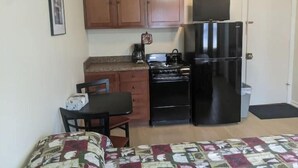 Une cuisine de taille réduite, avec des meubles en bois, un réfrigérateur noir, une cuisinière et une machine à café.