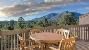 Una terraza de madera con una mesa redonda y sillas, con vistas a un paisaje montañoso con árboles.
