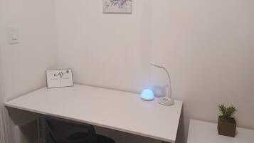 A white desk with a laptop, a white lamp, a sign with 'wifi password', and a small plant.