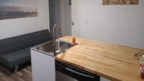 A compact kitchen with a wooden countertop, a built-in dishwasher, and a grey sofa. - Global Bed & Breakfast (Pottsville)