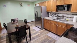 Eine kompakte Küche mit Holzschränken, einem Edelstahl-Kühlschrank, einer Mikrowelle und einer Arbeitsplatte aus Granit.