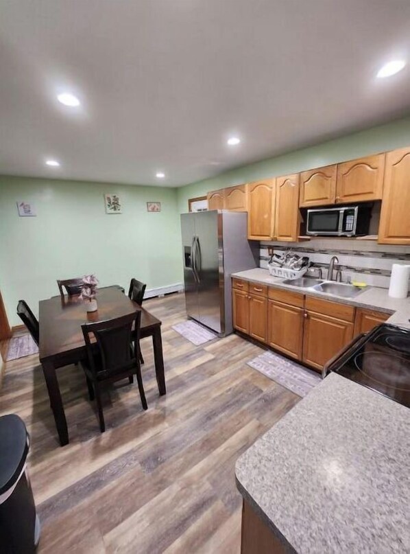 A compact kitchen with wooden cabinets, a stainless steel refrigerator, a microwave, and a granite countertop.