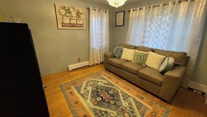 Ein Wohnzimmer mit einem braunen Sofa, einem gemusterten Teppich und einer Chandelier.