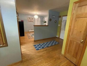 A hallway with wooden flooring, a blue patterned rug, a wooden door, and a light fixture on the ceiling.