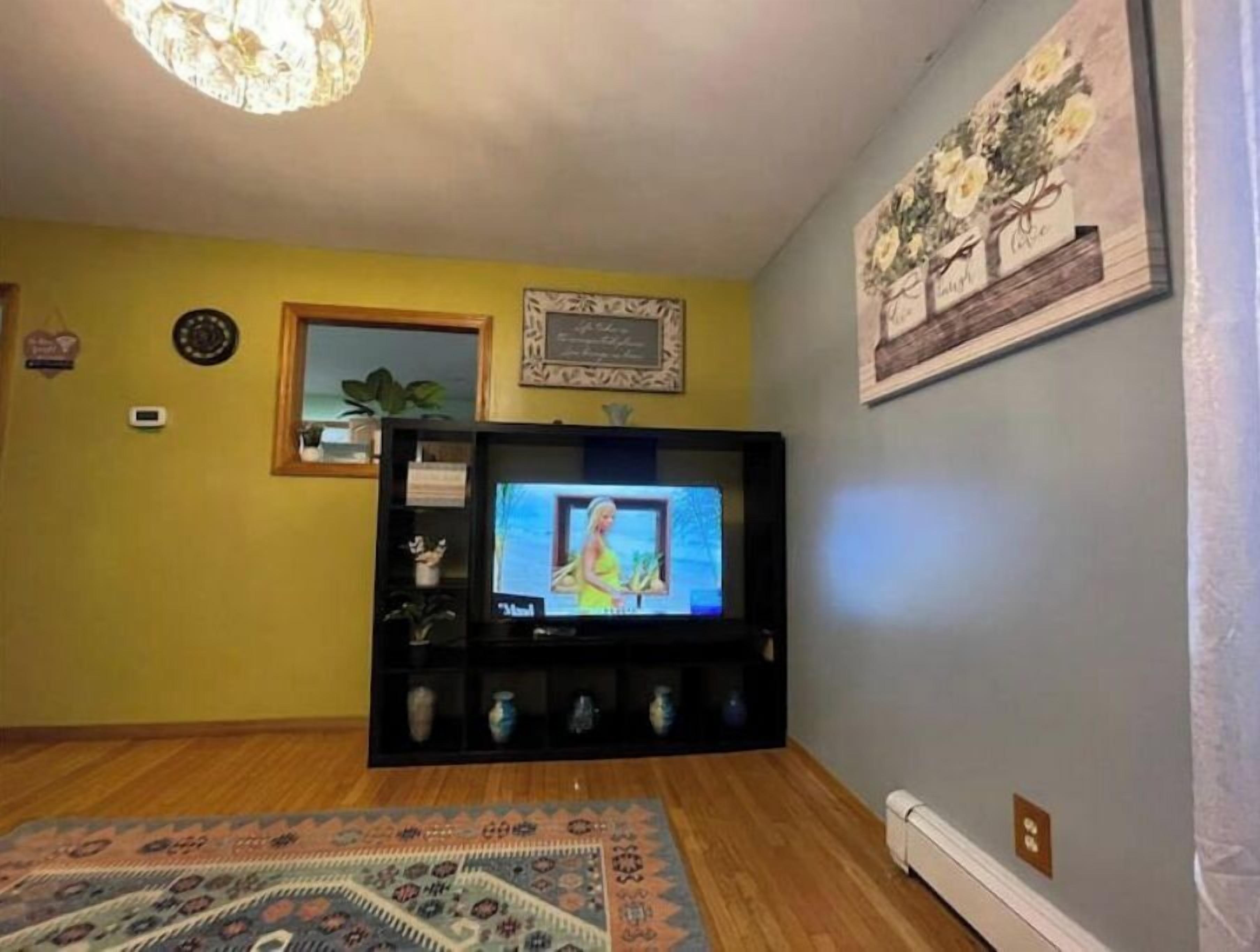 Una sala de estar con televisor, un espejo decorativo, una cita enmarcada y una alfombra estampada.