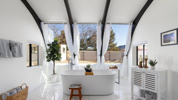 Ein modernes Badezimmer mit einer freistehenden Badewanne, einem weißen Waschtisch und einem großen Fenster mit Blick ins Freie.