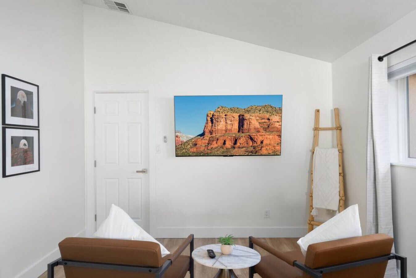 Una habitación con dos sillones de cuero marrón, una mesita redonda con una planta, un cuadro con una imagen de un cañón y una escalera apoyada en la pared.