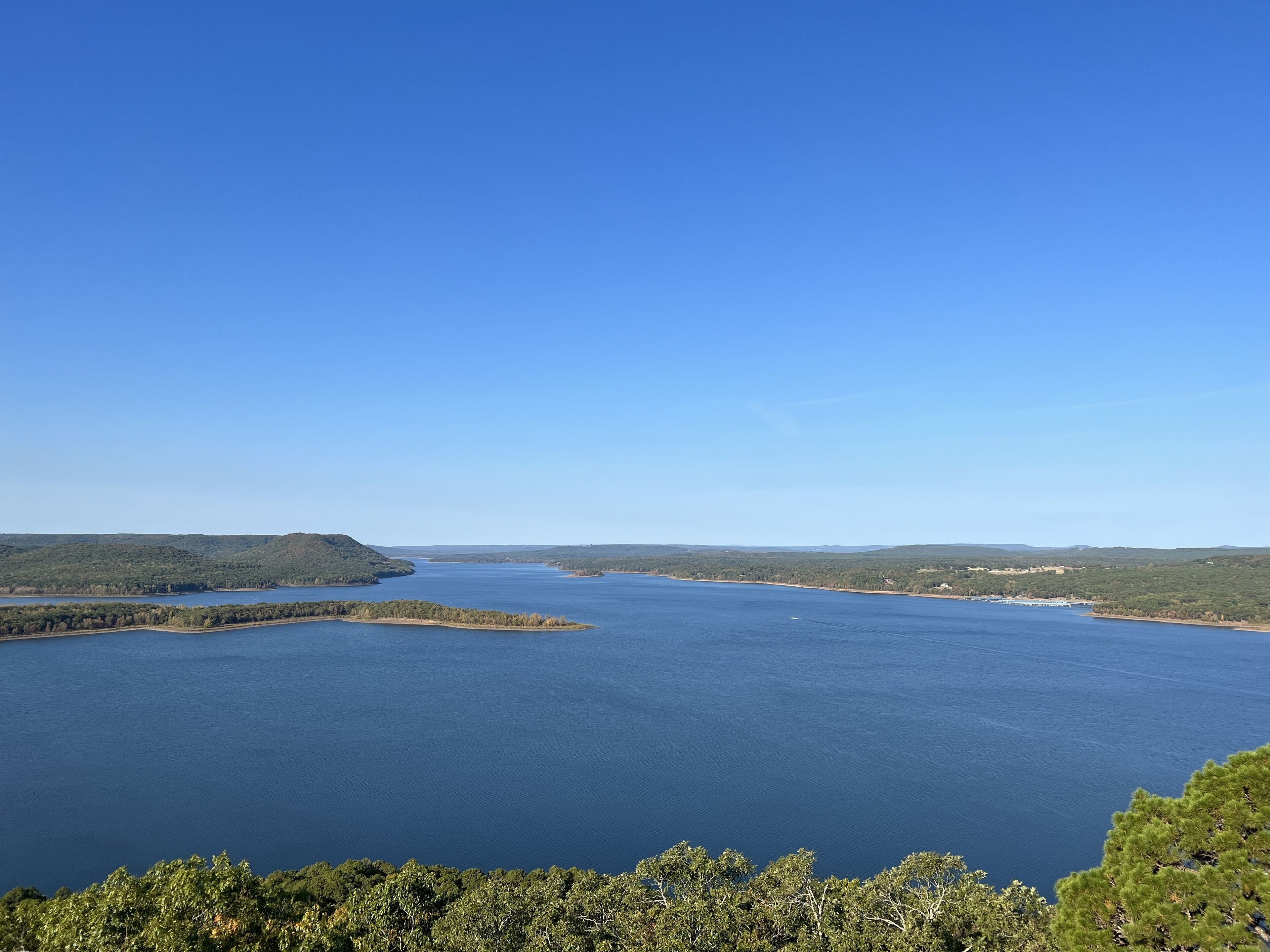 A panoramic view of a large body of water surrounded by hills and dense greenery.