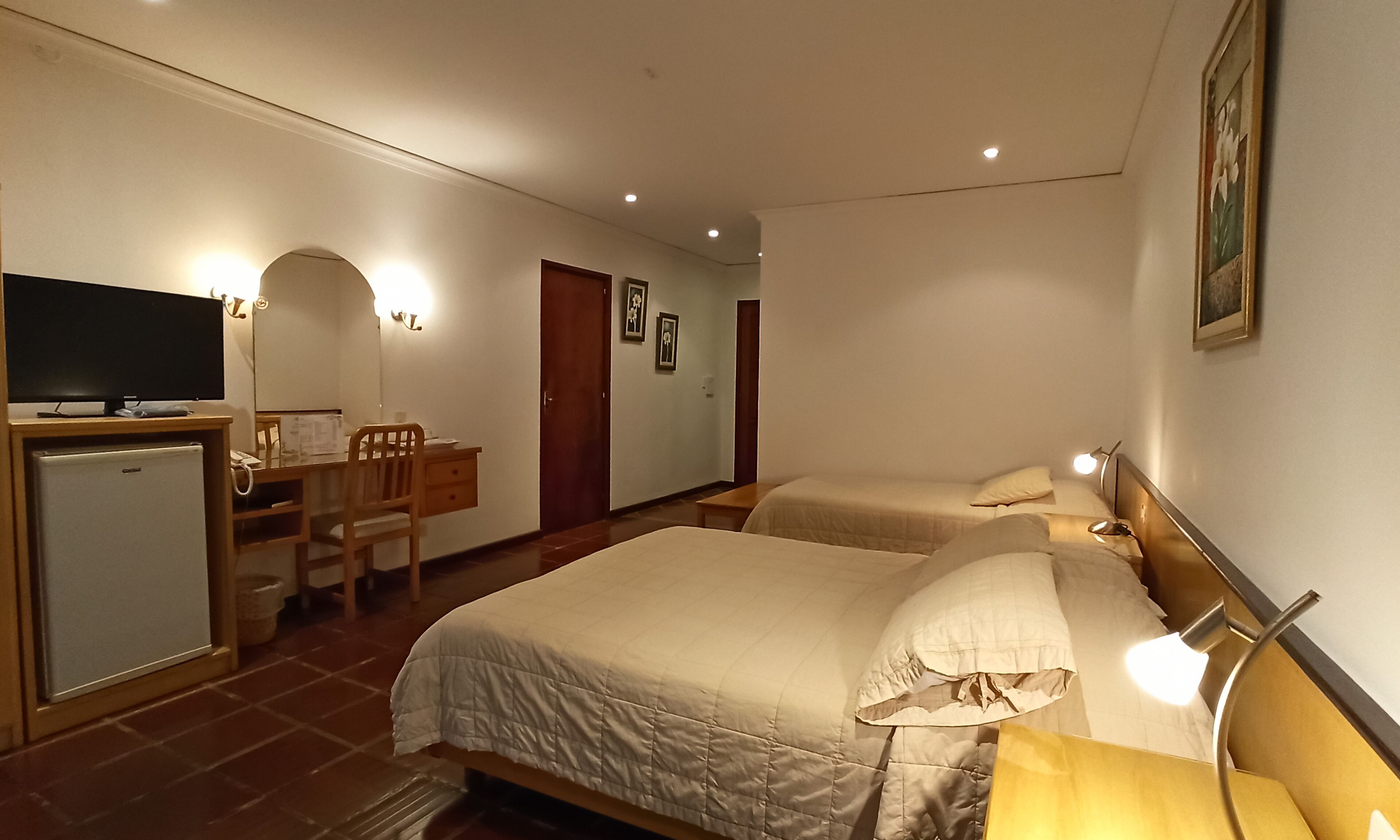 Ett hotellrum med två sängar, ett skrivbord med en dator, en tv och ett litet kylskåp.