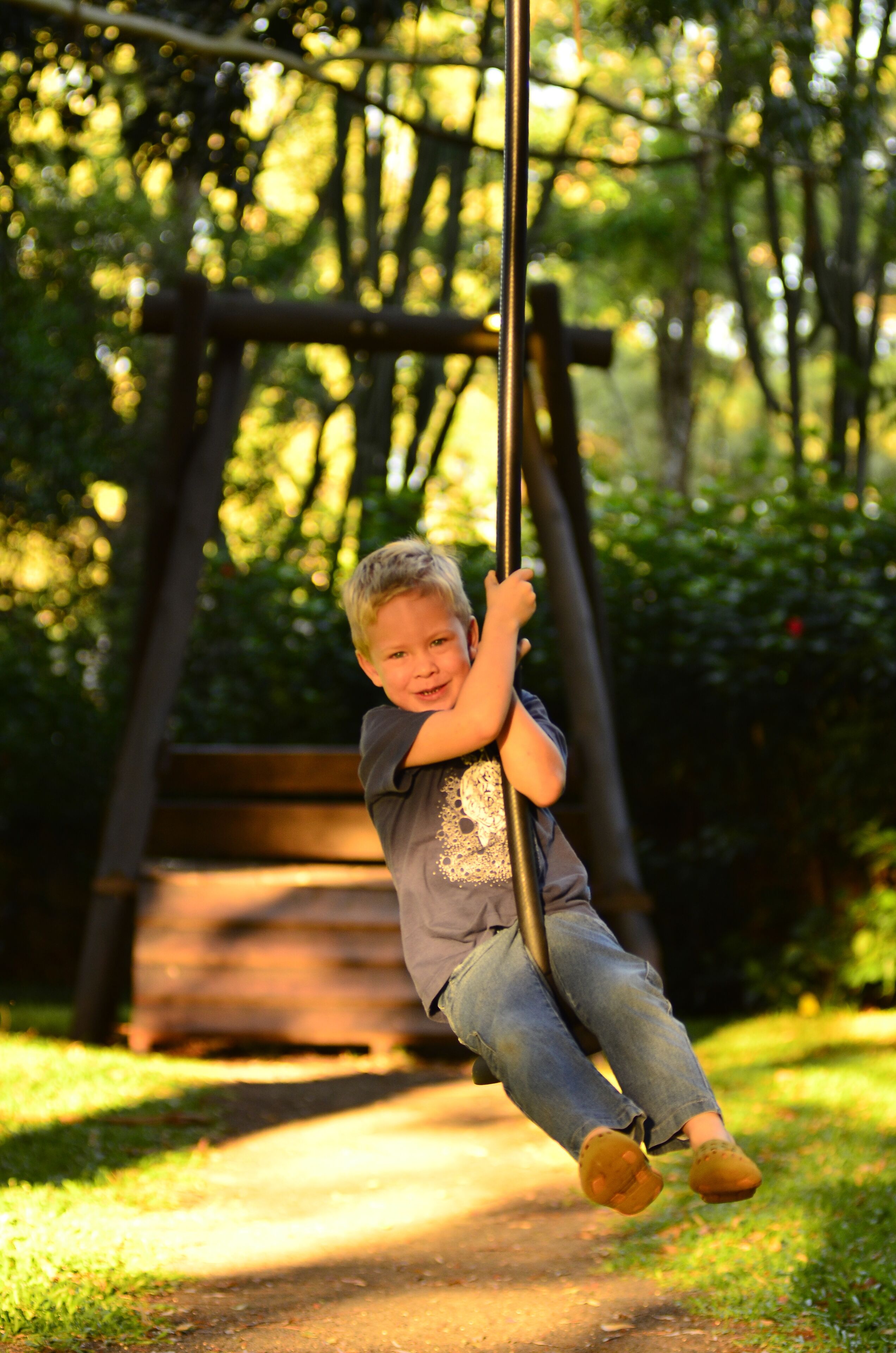 A child swinging on a swing set in a park with a wooden bench in the background.
