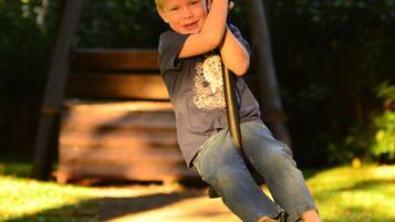 A child swinging on a swing set in a park with a wooden bench in the background.