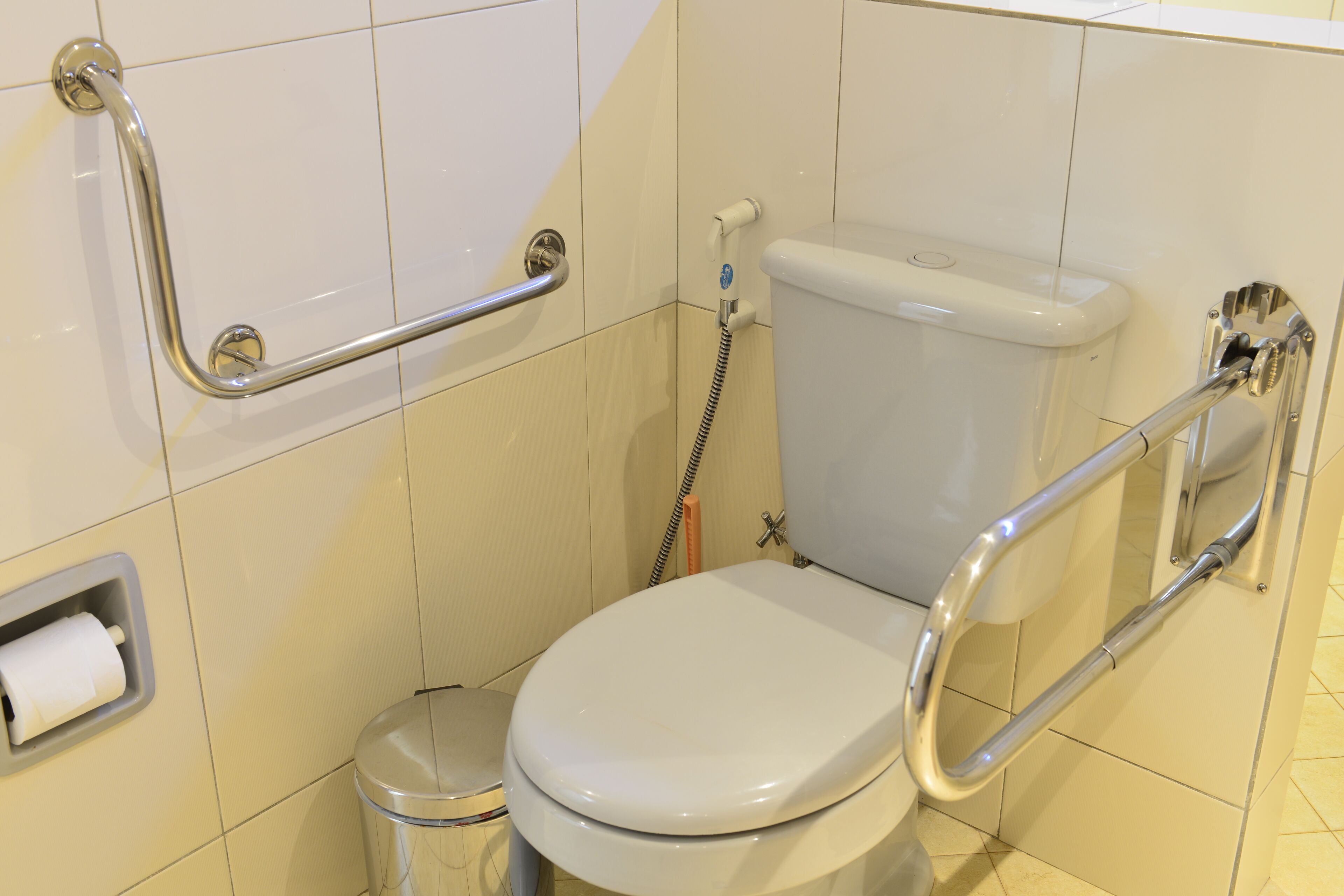 Un baño con inodoro blanco, barra de apoyo y cubo de basura.