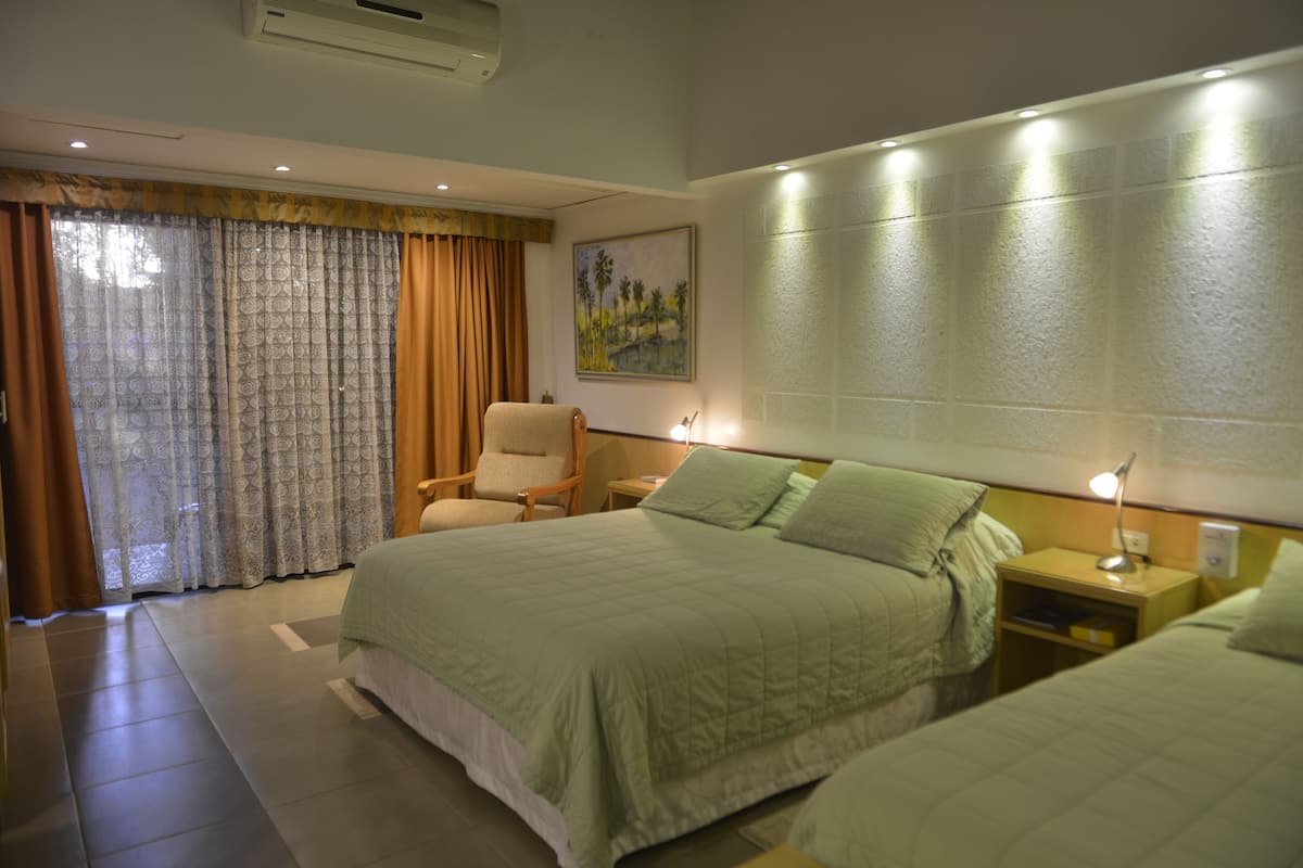 Habitación de hotel con una cama grande, una silla, una mesita de noche y un cuadro en la pared.