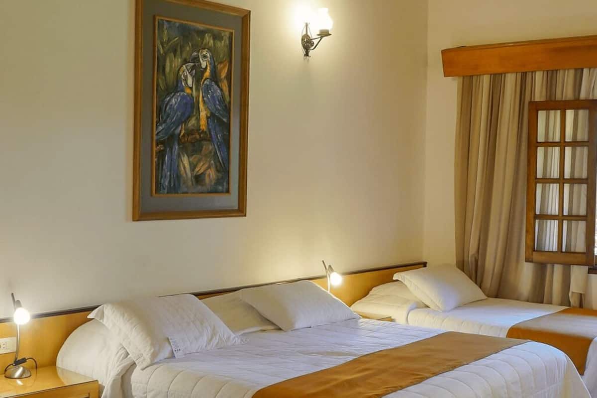 Una habitación de hotel con tres camas, un cuadro en la pared y una ventana con cortinas.