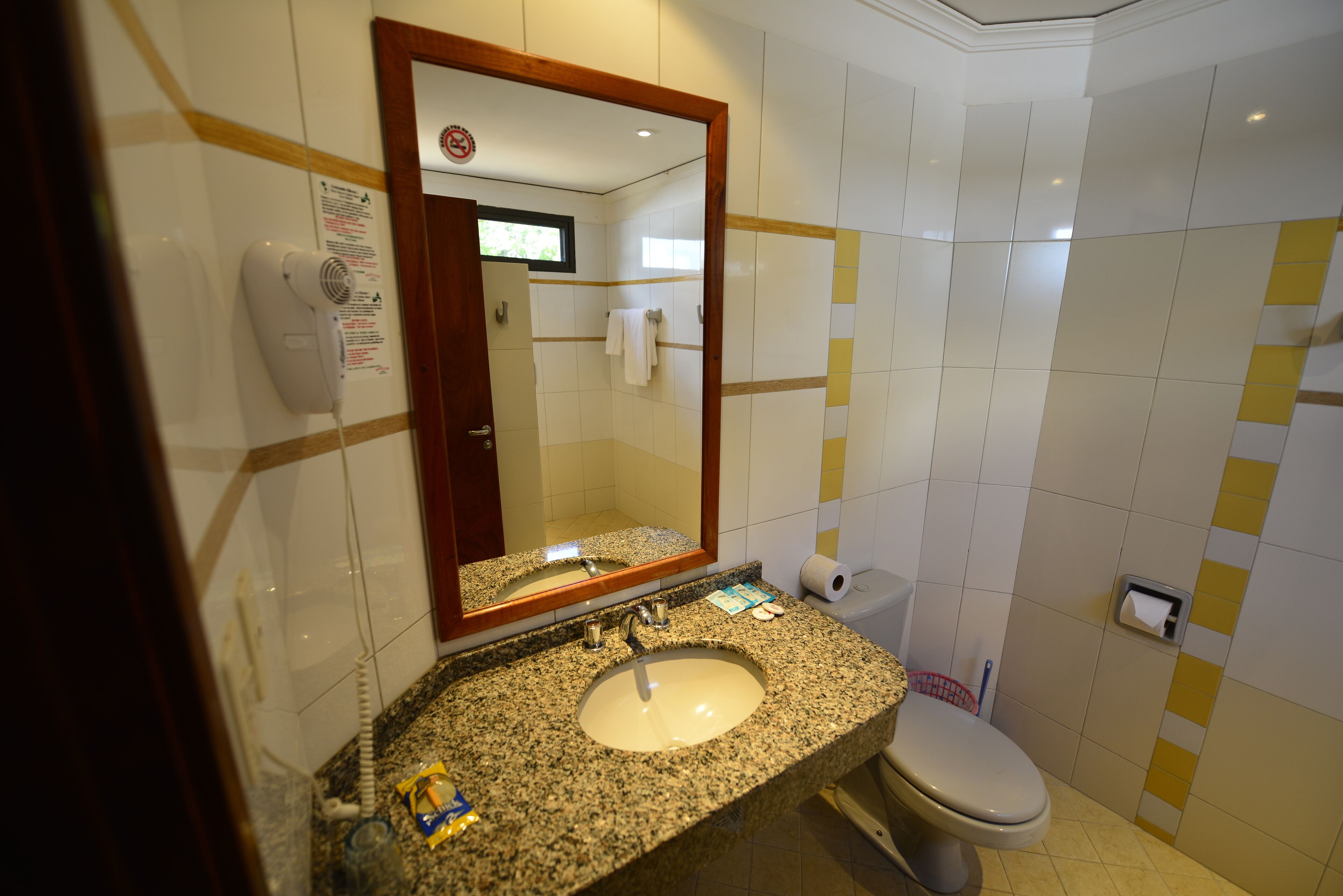 Un baño con lavamanos de granito, un espejo, un inodoro y un secador de manos.