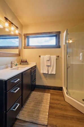 A modern bathroom with a glass shower, a vanity with a sink and mirror, and a window above the mirror.