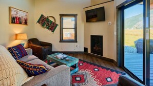 A cozy living room with a fireplace, a large window, and a view of the outdoors. - Blaine Cabin-Stunning Mountain Views,Close to GNP! (Columbia Falls)