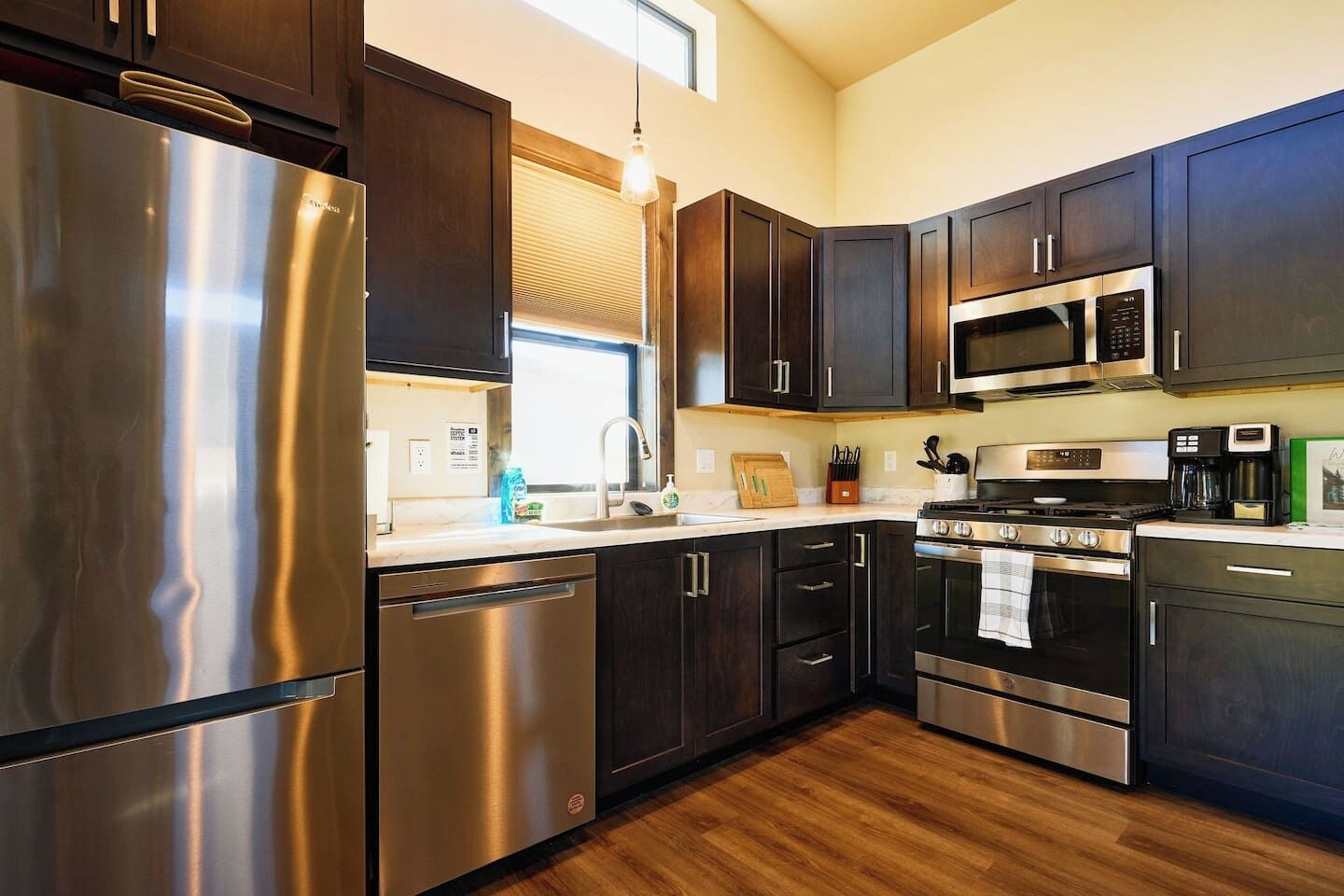 A modern kitchen with stainless steel appliances, dark cabinetry, and a wooden floor.