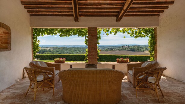 A covered patio with wicker furniture, a brick column, and a view of a green landscape. - Villa Montelisi, With The most Unique View On Siena (6km) (Siena)