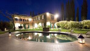 Zona de piscina con piscina, sillas de descanso y un edificio bien iluminado con balcón.