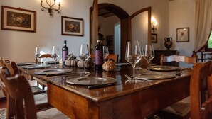 Una mesa de comedor de madera dispuesta con copas de vino, platos y cubiertos, con una araña y cuadros en las paredes.