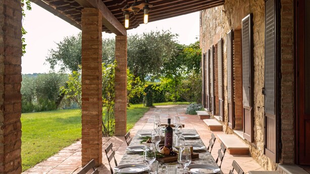An outdoor dining area with a table set for a meal, surrounded by brick walls and a garden view.