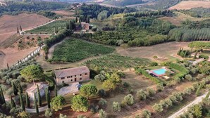 An aerial view of a rural property with a large stone building, vineyard, and swimming pool.