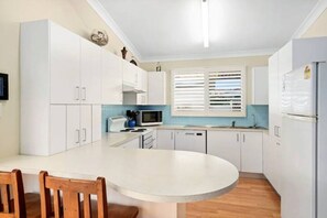 A compact kitchen with white cabinets, a microwave, a sink, and a refrigerator. - GoneToTheBeach - Beach, Spa, Pool table, Pets, Boards, Rods, Bikes. 
 Awesome. (The Entrance North)