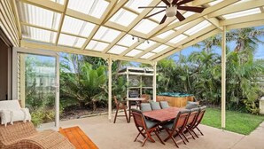 A covered patio with a wooden table and chairs, a grill, and a hammock.