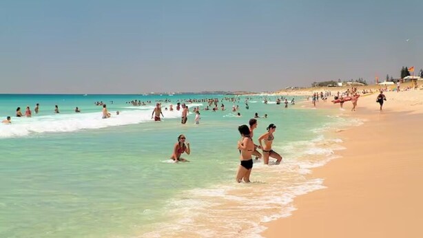 A crowded beach with people in the water and on the sand.