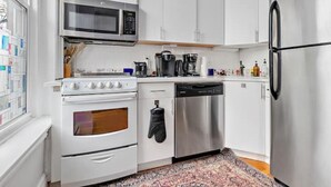 A modern kitchen with white cabinets, stainless steel appliances, and a patterned rug. - Historic Somerville Cambridge 1 Bed, Inman Square (Somerville)