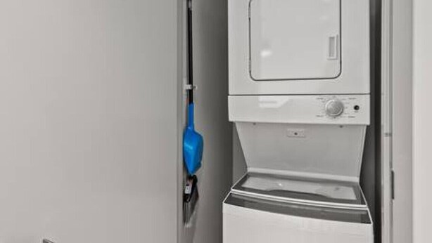 A compact, modern laundry room with a built-in washer and dryer, a blue mop, and a door handle. - 175 LEX - Walkable Downtown Lexington - Top Floor (Lexington)