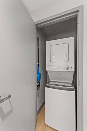 A compact, modern laundry room with a built-in washer and dryer, a blue mop, and a door handle.