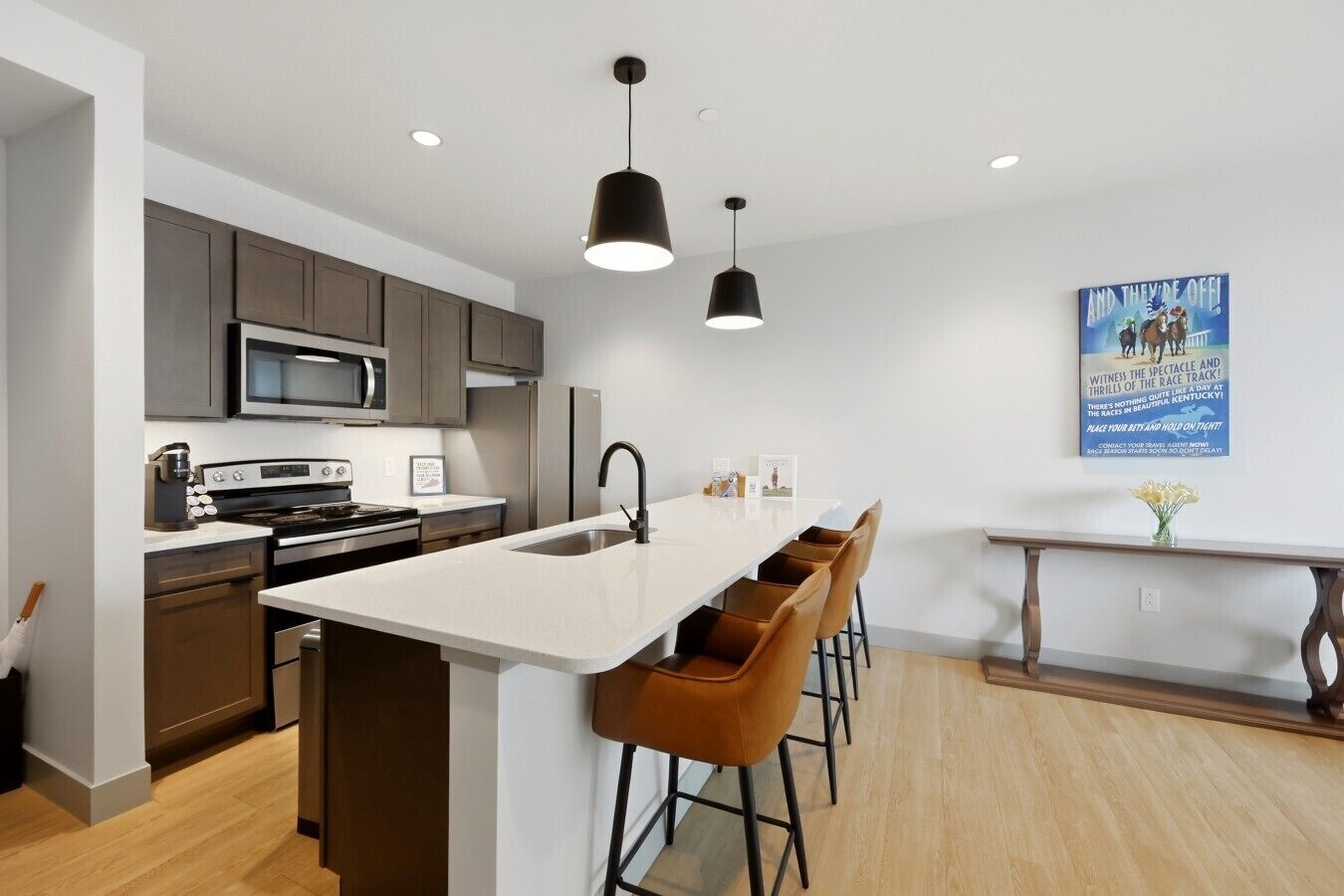 A modern kitchen with a central island, bar stools, a microwave, and a refrigerator.