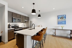 A modern kitchen with a central island, bar stools, a microwave, and a refrigerator. - 175 LEX - Walkable Downtown Lexington - Top Floor (Lexington)