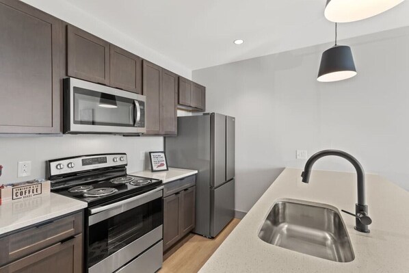 A modern kitchen with stainless steel appliances, a black faucet, and a pendant light.