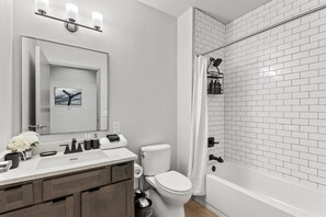 A modern bathroom with a white sink, mirror, and toilet, a shower with a white curtain, and a tiled wall. - 175 LEX - Walkable Downtown Lexington - Top Floor (Lexington)
