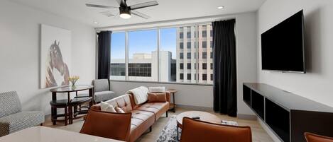 A modern living room with a sofa, chairs, a dining table, a TV, and a ceiling fan.