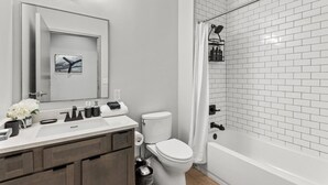 A modern bathroom with a white sink, toilet, and bathtub, featuring a tiled shower area and a mirror with lights. - 175 LEX - Walkable Loft to Rupp Arena & Downtown! (Lexington)