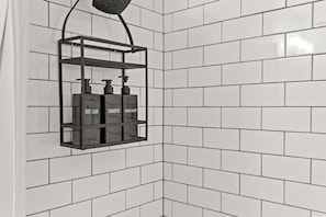 Une petite salle de bain avec des murs carrelés de blanc et une étagère noire où sont rangés les articles de toilette.