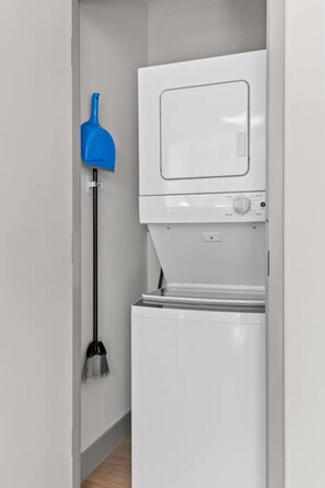 A compact, white laundry room with a built-in washing machine and dryer. A blue mop is mounted on the wall to the left.