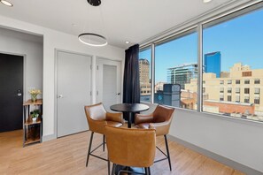 Ein modernes Zimmer mit einem runden Tisch und Ledersesseln, einem großen Fenster mit Blick auf die Stadt sowie einer Tür mit einer kleinen Ablagefläche.