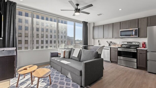A modern apartment with a grey sofa, a small wooden table, a kitchen with grey cabinets, a microwave, and a stove. - 175 LEX - Loft in Downtown Lexington, Rupp Arena (Lexington)